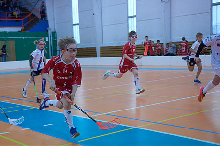 Children boys schoolchildren playing floorball (floor hockey) match in school gym sport hall with plastic hockey sticks